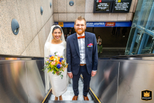 At a metro exit in Toulouse, Haute-Garonne, this high-angle shot captures the soon-to-be-married couple on their way to their wedding, both smiling directly at the camera, conveying excitement and urban charm.