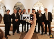A bridesmaid uses her phone to photograph the groom and his groomsmen at Le Tesserae in Houston, Texas, digitally preserving fun and friendship among the wedding party.