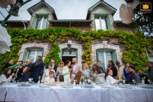 At an outdoor reception venue in Ille-et-Vilaine, Brittany, all the wedding guests raise their glasses at the table for a toast to the couple before lunch, filling the space with warm wishes and celebratory laughter.