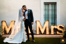 A Large Lit Sign Backdrops A Romantic Countryside Couple Portrait At Tenuta Acquaviva Travagliato At Tenuta Acquaviva in Travagliato, the newlyweds share a quiet, romantic portrait session together outdoors with a large, lit 'Mr & Mrs' sign, the Italian countryside providing a picturesque backdrop as they pause to embrace amid the festivities.