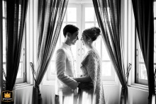 A black-and-white portrait at Baan Dusit Thani in Bangkok, Thailand, shows the couple standing symmetrically before windows with drawn-back curtains, creating a refined image defined by balance, light, and architectural elegance.
