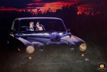 The newlyweds pause inside a vintage wedding car in Bucharest, Romania, as the last light of sunset colors the sky, creating a cinematic scene between celebration and romance.