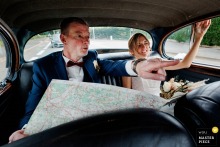 The groom is seen in the backseat of the car, directing the driver with a paper map while the bride sits beside him in this auto wedding image, created near Domaine des sources