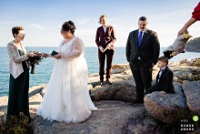 At Acadia National Park in Maine, during an elopement ceremony, the couple stands on the rocks by the ocean. It's a sunny day, and the ocean nearby, adding to the beauty of their day.