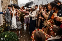 Amid a rain shower at Sheffield Manor Lodge in Sheffield, England, the bride and groom are joyfully showered in vibrant confetti by their wedding guests.