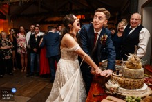 Bride and groom at Hobbit Hill, Lancashire, cut whimsical cheese cake, both laughing, surrounded by rustic wedding décor and guests.