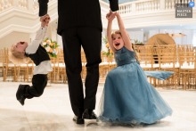 Children laugh and playfully hang from a man's hands at the National Museum of Women in the Arts wedding event.
