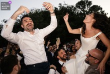 At Vandelli Garden, the bride and groom are joyfully lifted into the air by guests during a lively cocktail hour celebration.