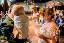 In Plein 7, Woerden, groom holds son while exchanging vows. Son plays with toy car on mother's face, creating smiles.