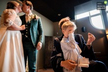   Inside wedding venue Plein 7 in Woerden, the ring bearer rubs his eye as the couple shares a kiss and the officiant presents their wedding ring.