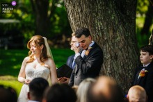Groom Wipes Away Tears During Outdoor Ceremony Reading at Liberty View Farm, New York Wedding At Liberty View Farm in New York, a groom wipes away tears during a reading at an outdoor wedding. The award-winning photograph highlights the photographer's skill at documenting the emotional moments of a ceremony.