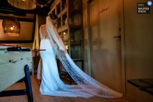 Bride Smiles And Laughs Freeing Veil From Door At Château De Chignat France At Château de Chignat, France, the photographer captures the bride smiling and softly laughing as she gently frees her veil from a door, showcasing a tender, candid moment and exceptional storytelling skill.