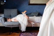 Little Girl Watches Bride Get Dressed At Home In 's-Hertogenbosch Noord Brabant Pre-Wedding Moment At home in 's-Hertogenbosch, Noord Brabant, the photographer captures a little girl lying on the couch watching the bride get dressed, beautifully highlighting quiet anticipation and skilled storytelling in a candid pre-wedding moment.