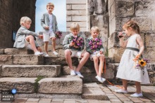 At Eglise d'Urrugne in Pyrénées Atlantiques, France, the photographer captures the young attendants waiting patiently on the church steps after the religious ceremony, highlighting composed innocence and skillful storytelling.