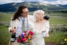 At Yellowstone, the photographer captures a tender scene as the groom wraps his arm around the bride, both dressed in white, sharing champagne and a quiet, intimate celebration, emphasizing timing and gentle emotion.