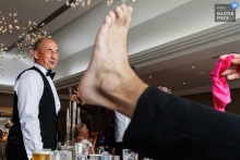 At Crow Wood in Lancashire, England, the photographer captures a playful reception moment as guests enjoy games, focusing on a man’s sour expression and a bare foot filling the foreground, highlighting creative framing and spontaneous humor.