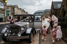 At St. Mary’s RC Church in Lancashire, England, the photographer captures the bride’s arrival in a vintage limo amid an urban street scene, elegantly blending anticipation and classic wedding style with expert storytelling.