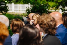 During a poignant ceremony in Highland, New York, the mother of the bride tenderly wipes away tears of joy while watching her daughter exchange vows in an emotional setting.