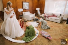 At Mission Viejo Country Club, a bride snaps a photo as friends cut her dress and her brother naps, showcasing the photographer’s artistry in capturing layered, storytelling moments within one vibrant scene.