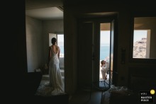 In Santorini, Greece, the bride prepares in the bathroom while the groom waits outside, carefully avoiding a glimpse to keep the wedding day surprise.