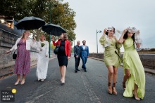 In Paris, France, rain falls on the wedding day as two bridesmaids walk outside without umbrellas, highlighting a candid and lighthearted moment amid the celebrations.