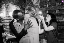Lyon, Rhône Wedding Reception Kiss Candid at Venue Filmed by Witness At a reception venue in Lyon, Rhône, the bride and groom share a spontaneous kiss at the start of the meal while a witness on the right quickly films the scene, preserving the joyful moment.