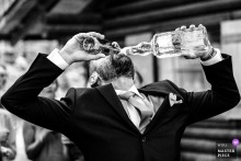 At the wedding party, a man pours both beer and aims into his mouth simultaneously. Captured in black and white, the shot exudes playful energy.