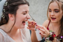 At Danzturm Iserlohn in Germany, the bride’s hair becomes tangled in a spinning hand fan, prompting a quick rescue by the maid of honor—a candid moment capturing laughter, teamwork, and the unpredictability of wedding day preparations.