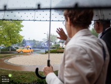 A yellow quirky car pulls up to city hall in Ille-et-Vilaine, Brittany, with guests inside waving and greeting friends, all while a light rain falls outside.