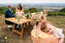 Mom And Dad Sign Marriage Paperwork At Hilles House Gloucestershire England At Hilles House in Gloucestershire, England, Mom and Dad sign the wedding paperwork while a woman holds a sleeping baby in the foreground, capturing a tender blend of official ceremony and family life.