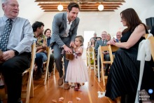 A tender scene captured at a Santa Barbara Central Coast church, as a reluctant flower girl is gently guided up the aisle by a helpful man. Photographed from a low angle, the moment highlights her shyness and support.