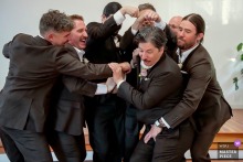An energetic and wild moment inside a Santa Barbara Central Coast church, as a boisterous group of men humorously swarm and grab the groom, capturing the playful chaos and camaraderie among friends during the wedding celebration.