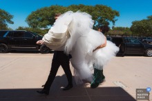 A humorous moment captured at Mater Dei Catholic Church in Chula Vista, California, as the bride's dress is transported by her sister and her boyfriend, the gown billowing like a cloud walking with legs.
