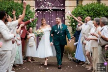   Friends and family create a guard of honor as the newlyweds leave the town hall, their joyful exit marking a highlight of the ceremony’s conclusion.