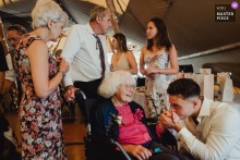   A tender gesture unfolds at the reception in Kent as the bride’s son leans in to kiss his grandmother’s hand, expressing love and connection across generations.