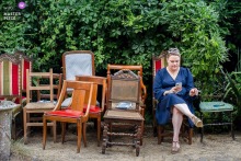   In Largentiere, France, a woman sits alone outside surrounded by well-worn old chairs, adding character and a touch of nostalgia to the elegant wedding setting.