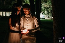   Deep in the forest near Geneva, Switzerland, the couple stands illuminated by a single lamp, creating a serene and symbolic nighttime atmosphere.