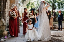   A flower girl mischievously pulls on the bride’s veil during the ceremony at Holy Trinity Church in Stratford Upon Avon, England, endearing guests with a sweet and candid wedding moment.