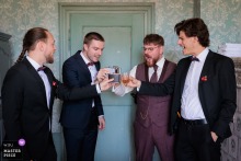 At the reception location in Hérault, France, the groom toasts with whisky beside his best men and groomsmen, a last pocket of calm before the ceremony begins.