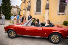 The bride in a red convertible sports car in Goutz, Gers, France arrives like a flash of color against softer tones, the vehicle adding motion, style, and a hint of drama.
