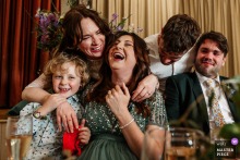 When the speeches end at Dorothea Village Hall in Warwickshire, England, laughter and embraces rise around the bride, a soft, relieved rush of affection everywhere.