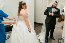 At Vellano Estate in Chino Hills, California, the groom tries on the bride’s veil while she is bustled for the reception, a playful exchange between ornament and ceremony.