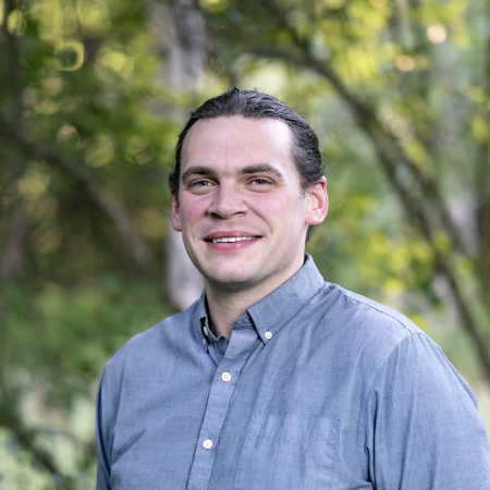 Josh Kuckens, a professional wedding photographer based in Vermont, stands smiling in natural light.