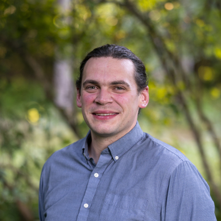 Josh Kuckens, a professional wedding photographer based in Vermont, stands smiling in natural light.
