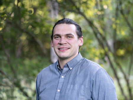 Josh Kuckens, a professional wedding photographer based in Vermont, stands smiling in natural light.