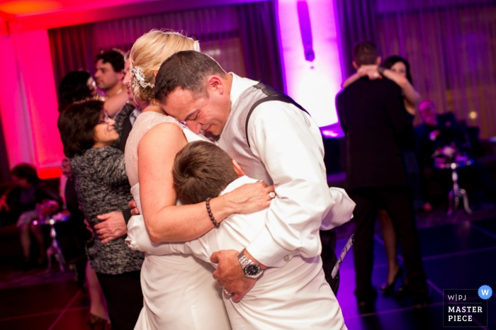 Nova Escócia noiva e noivo abraçam menino enquanto eles estão dançando - fotojornalismo de casamento no Canadá