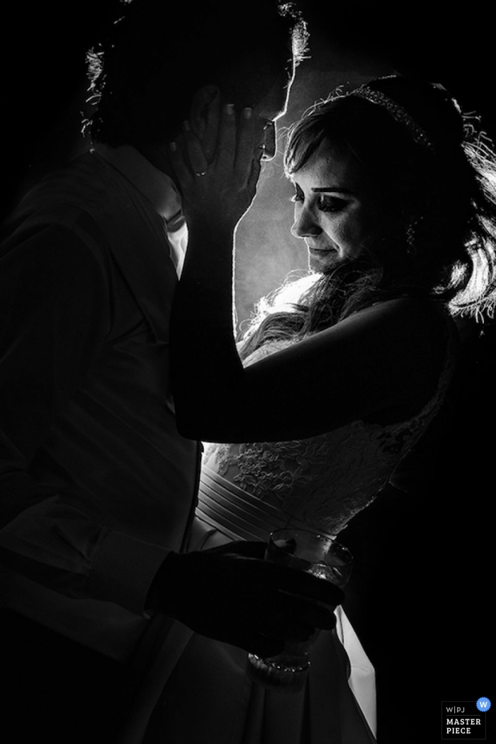 The bride puts her hand on the groom's face as they dance together during the reception in this black and white image by a Sao Paulo documentary wedding photographer.