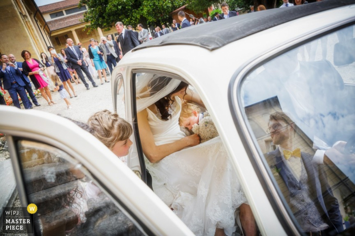 Na tym zdjęciu ślubnym skomponowanym przez weneckiego fotografa panna młoda siedzi na tylnym siedzeniu samochodu, a na niej śpi mały chłopiec.