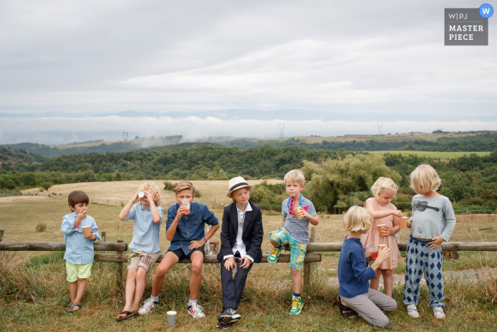 Foto von: <a href="https://www.wpja.com/contests/2016-q3-photography-contest/kids-being-kids/1922636"> Jacqueline Dersjant - Niederlande </a> Foto von den Kindern, die auf einem Zaun vor einem Feld von einem Amsterdam-Hochzeitsfotografen sitzen.