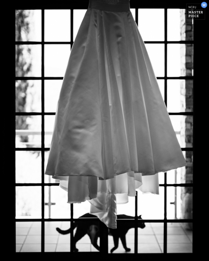 Photo détaillée en noir et blanc de la robe de la mariée accrochée à une fenêtre alors qu'un chat passe en dessous par un photographe de mariage à Porto, au Portugal.